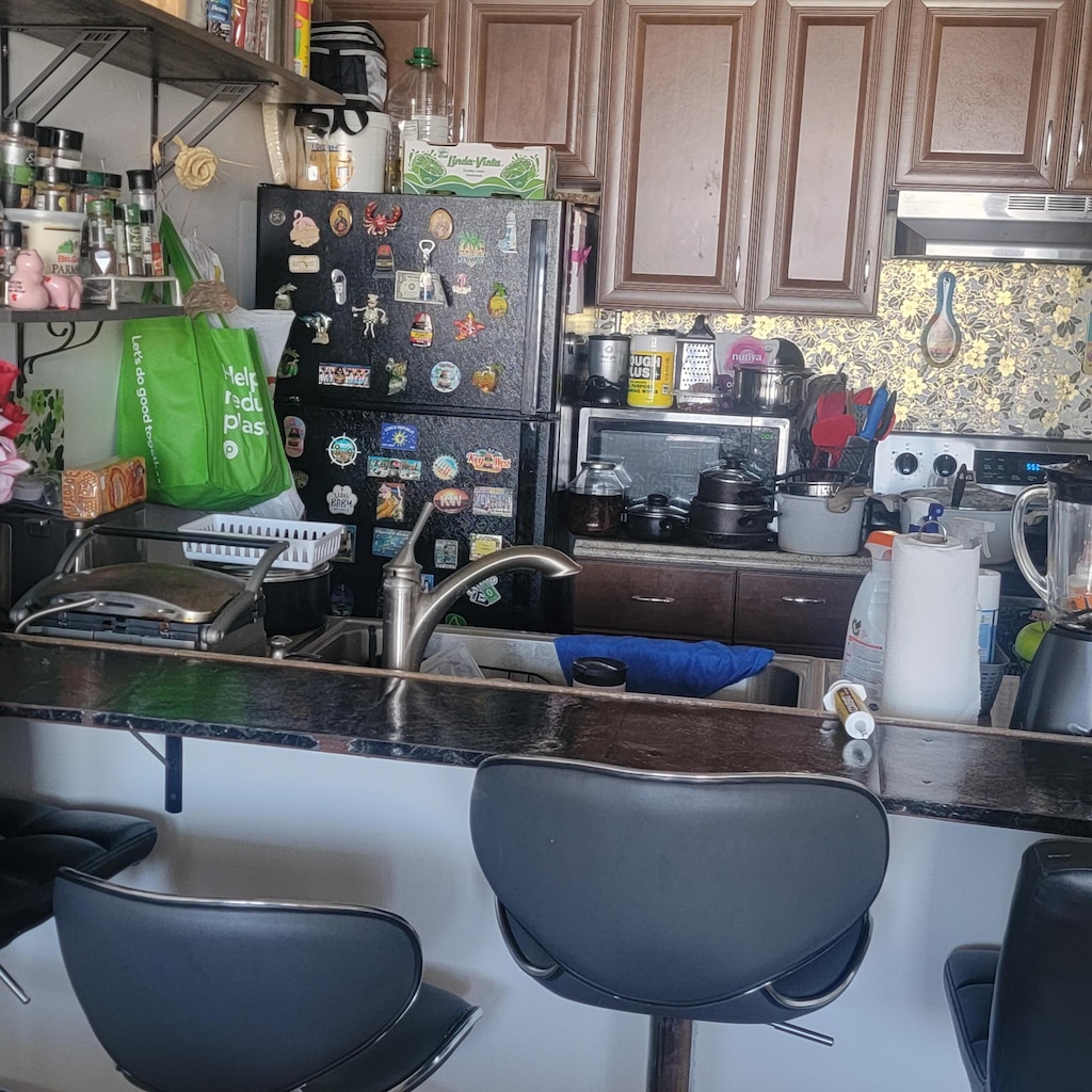 3312 Northside Dr Unit 407, Key West, FL 33040 - kitchen with under cabinet range hood, freestanding refrigerator, dark countertops, and backsplash