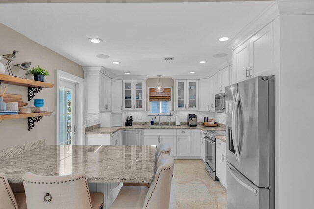 kitchen with appliances with stainless steel finishes, decorative light fixtures, sink, white cabinets, and a kitchen breakfast bar