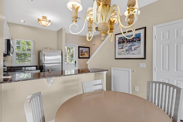 kitchen featuring dark stone countertops, a notable chandelier, and freestanding refrigerator