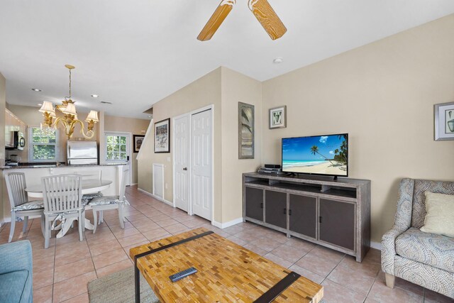 tiled living area featuring baseboards and ceiling fan with notable chandelier