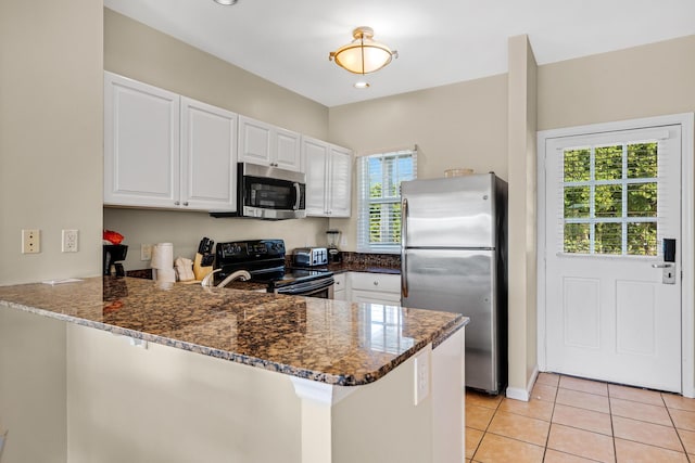kitchen featuring white cabinetry, stainless steel appliances, dark stone counters, a peninsula, and light tile patterned floors
