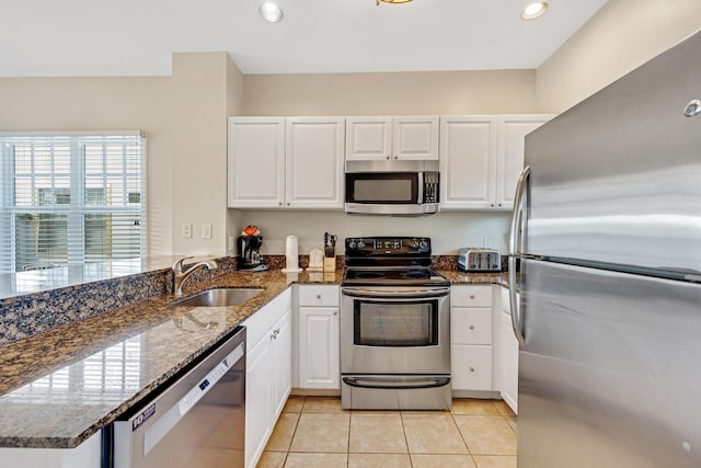 kitchen with a peninsula, stainless steel appliances, light tile patterned flooring, white cabinetry, and a sink