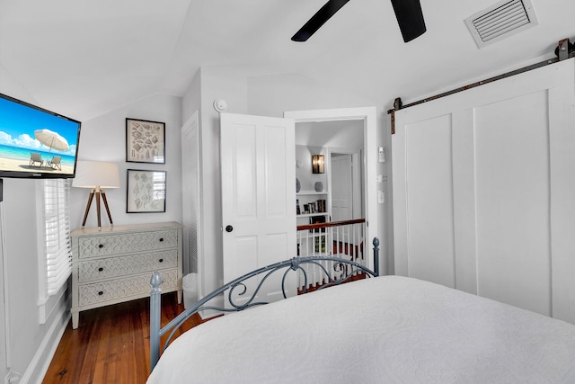 bedroom featuring dark hardwood / wood-style floors, ceiling fan, a barn door, and vaulted ceiling