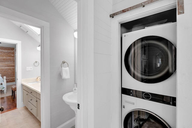 laundry area featuring light tile patterned flooring, stacked washing maching and dryer, sink, and wood walls