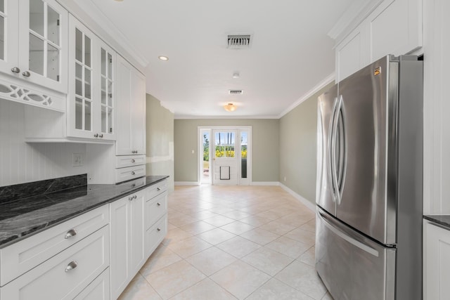 kitchen featuring stainless steel refrigerator, white cabinetry, dark stone counters, light tile patterned floors, and crown molding