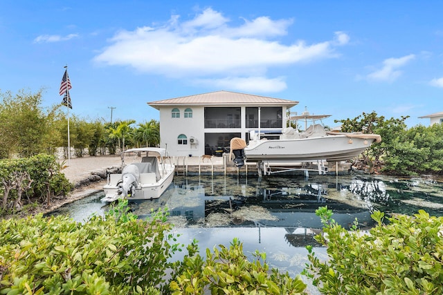 rear view of property featuring metal roof, boat lift, a water view, a sunroom, and a standing seam roof