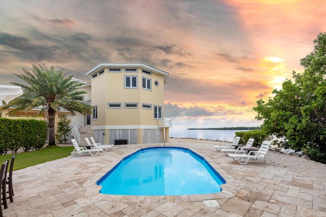 pool at dusk with a water view and a patio area