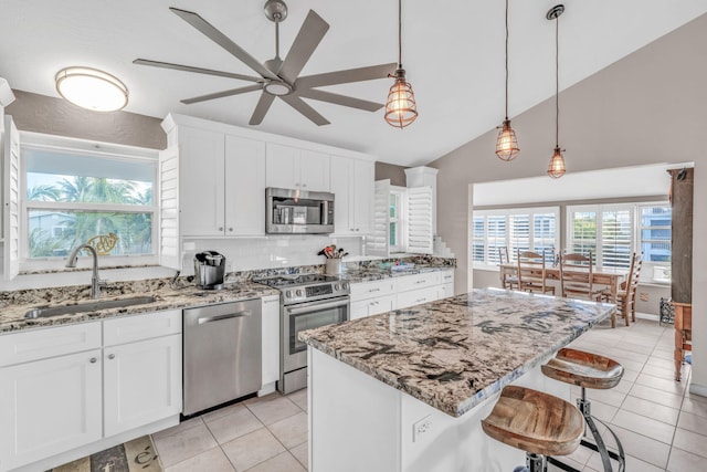 kitchen featuring sink, appliances with stainless steel finishes, light stone countertops, white cabinets, and a kitchen island