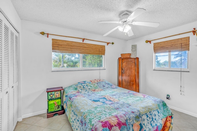 tiled bedroom with multiple windows, ceiling fan, a closet, and a textured ceiling