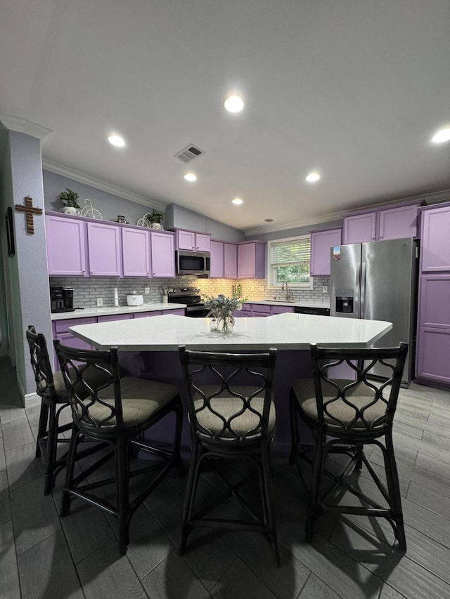 kitchen featuring sink, appliances with stainless steel finishes, a kitchen island, tasteful backsplash, and a kitchen bar