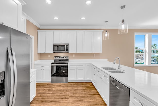 kitchen featuring light wood-style flooring, crown molding, a sink, appliances with stainless steel finishes, and pendant lighting