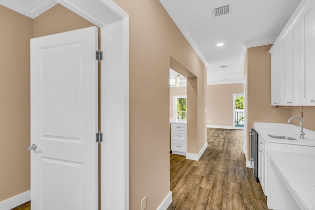 interior space with baseboards, dark wood finished floors, ornamental molding, white cabinetry, and a sink