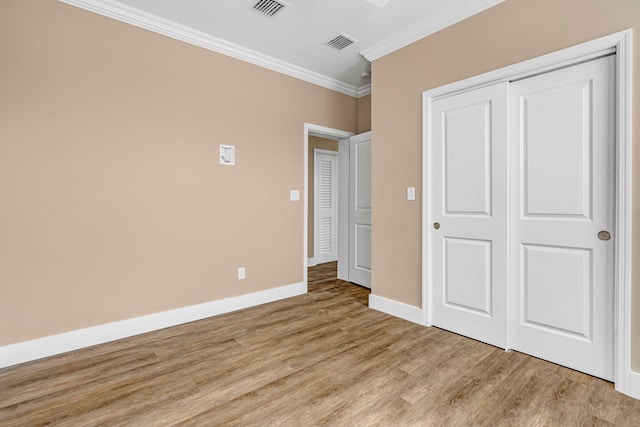 unfurnished bedroom with wood finished floors, visible vents, baseboards, ornamental molding, and a closet