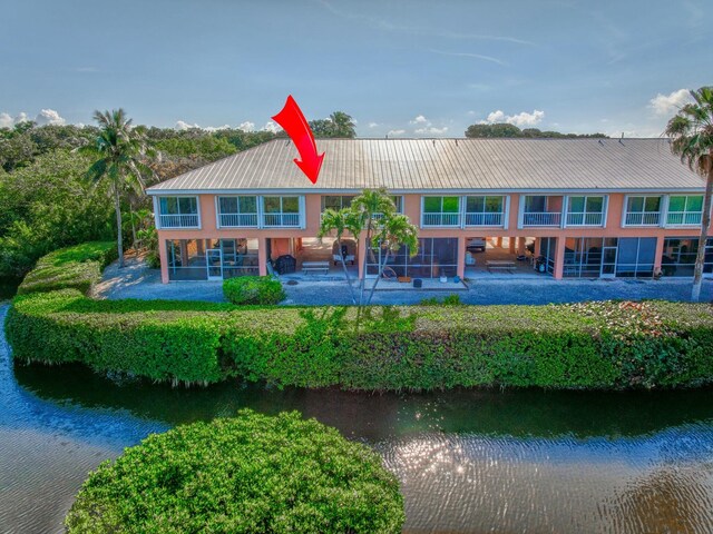 back of property with metal roof, a water view, stucco siding, and a patio