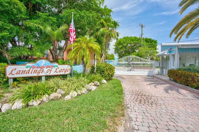 community sign with a gate, driveway, and fence
