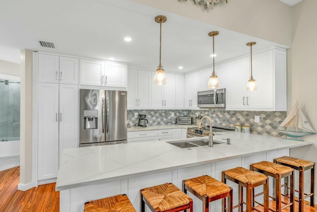 kitchen featuring light wood-type flooring, backsplash, appliances with stainless steel finishes, and a peninsula