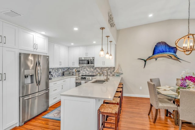 kitchen featuring a sink, a kitchen bar, a peninsula, stainless steel appliances, and visible vents