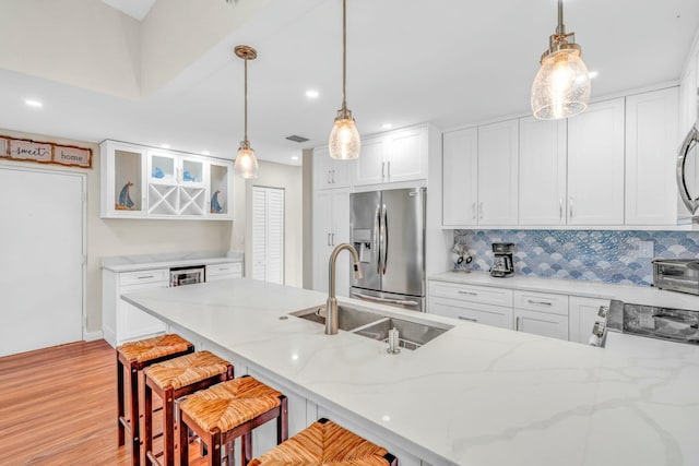kitchen with tasteful backsplash, stainless steel appliances, a sink, light wood finished floors, and a peninsula
