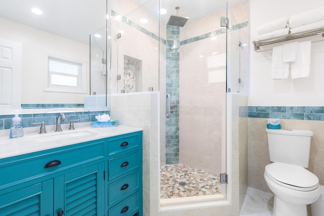 bathroom with vanity, toilet, a shower with door, and tile walls