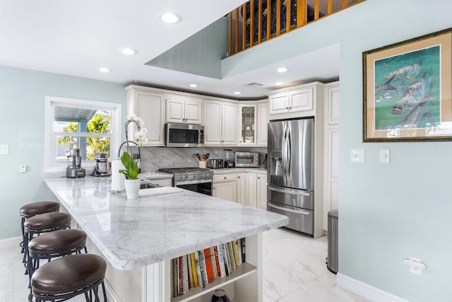 kitchen featuring appliances with stainless steel finishes, a kitchen breakfast bar, decorative backsplash, light stone counters, and kitchen peninsula