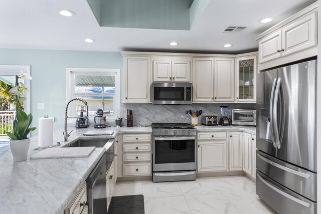 kitchen featuring stainless steel appliances, sink, backsplash, and light stone counters