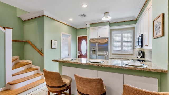 kitchen featuring light stone countertops, ornamental molding, stainless steel appliances, and white cabinets