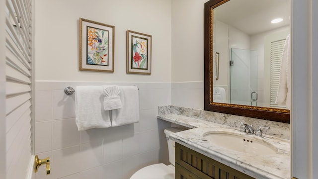 bathroom with a shower with door, vanity, tile walls, and toilet