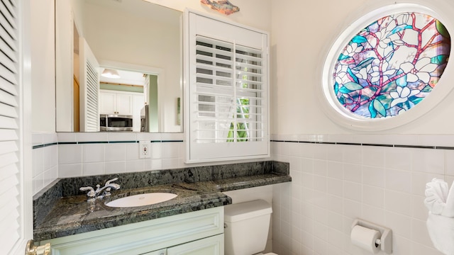 bathroom with vanity, toilet, and tile walls