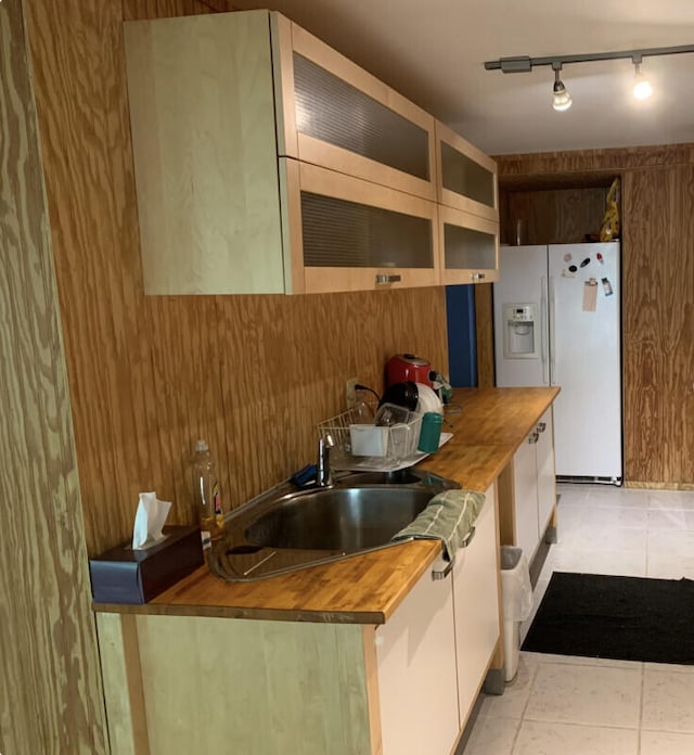 kitchen with light tile patterned flooring, sink, white cabinetry, wooden counters, and white fridge with ice dispenser