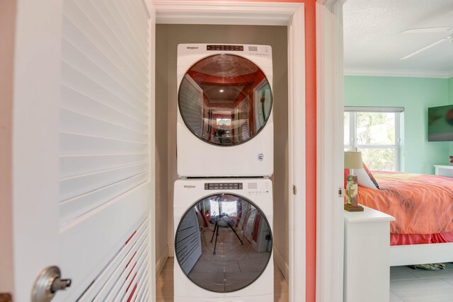 clothes washing area featuring crown molding, tile patterned floors, stacked washing maching and dryer, and a textured ceiling