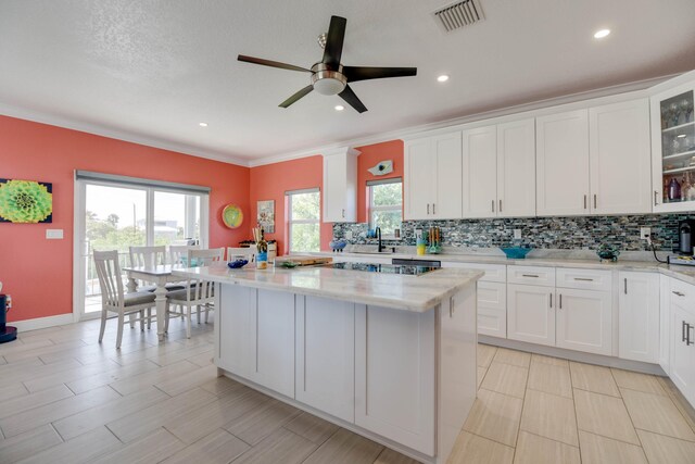 kitchen featuring sink, white cabinetry, a center island, light stone countertops, and backsplash