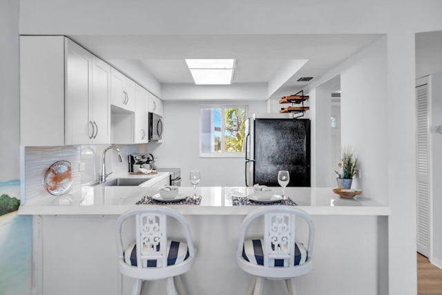 kitchen with a breakfast bar, sink, white cabinetry, appliances with stainless steel finishes, and kitchen peninsula