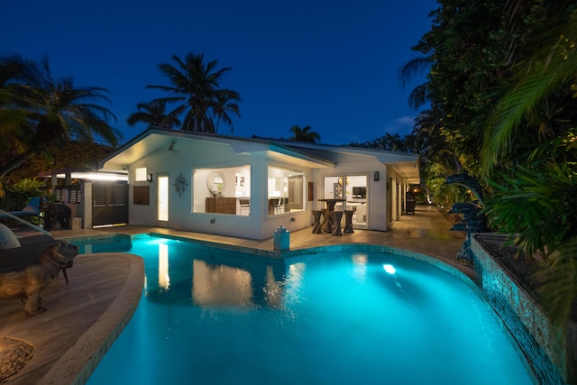 pool at night featuring an outdoor pool and a patio