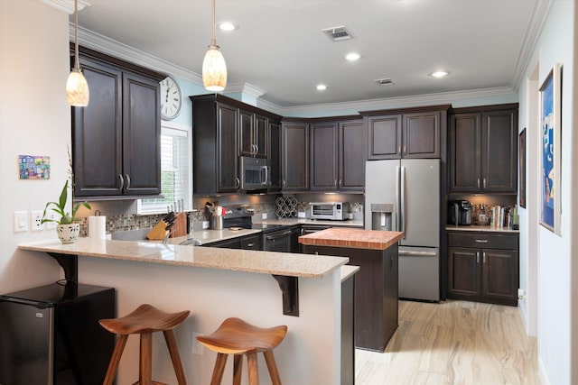 kitchen featuring appliances with stainless steel finishes, a kitchen bar, kitchen peninsula, and hanging light fixtures