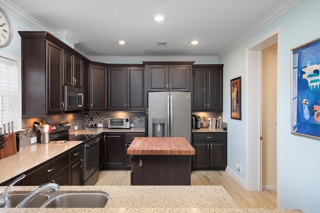 kitchen with a kitchen island, appliances with stainless steel finishes, sink, light stone counters, and dark brown cabinets