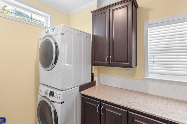 washroom with crown molding, cabinets, and stacked washing maching and dryer