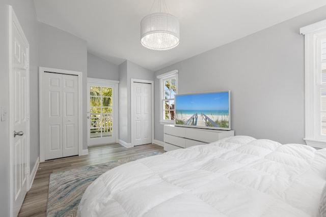 bedroom with multiple closets, vaulted ceiling, an inviting chandelier, and light hardwood / wood-style floors