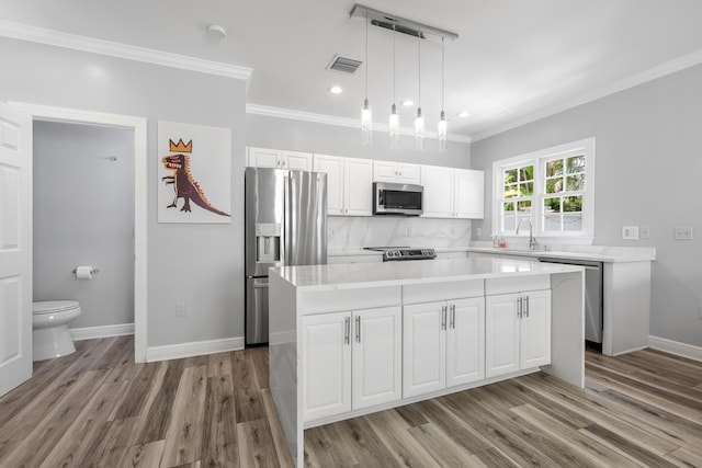 kitchen featuring appliances with stainless steel finishes, pendant lighting, white cabinets, decorative backsplash, and a center island