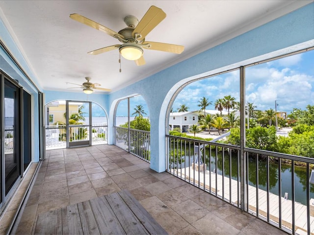 unfurnished sunroom featuring ceiling fan and a water view