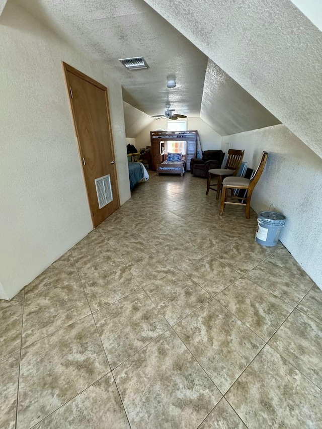 additional living space with lofted ceiling, visible vents, a textured wall, and a textured ceiling