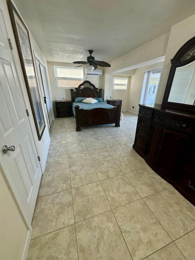 bedroom featuring light tile patterned floors, a textured ceiling, ceiling fan, baseboards, and an AC wall unit