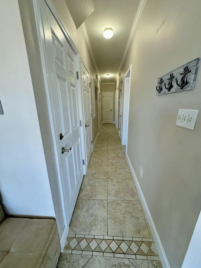 hallway featuring light tile patterned floors, baseboards, and crown molding