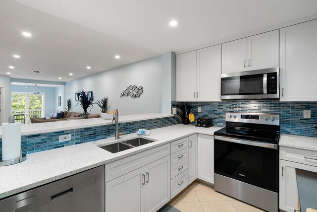 kitchen featuring sink, light tile patterned floors, appliances with stainless steel finishes, white cabinets, and backsplash