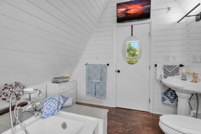 bathroom with a tub, wood walls, and toilet