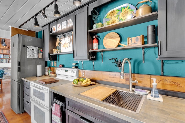 kitchen featuring sink, light hardwood / wood-style flooring, stainless steel fridge, rail lighting, and range with two ovens