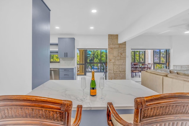 kitchen featuring light stone counters, stainless steel dishwasher, a healthy amount of sunlight, and gray cabinetry