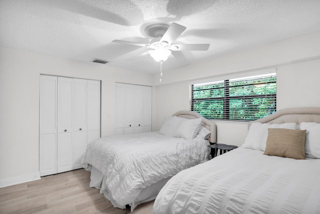 bedroom featuring ceiling fan, two closets, a textured ceiling, and light wood-type flooring