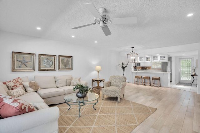 living room featuring ceiling fan with notable chandelier, a textured ceiling, and light wood-type flooring