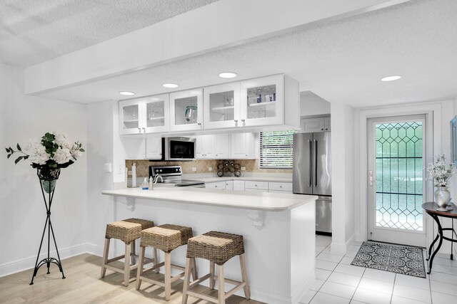 kitchen with tasteful backsplash, white cabinets, kitchen peninsula, stainless steel appliances, and a textured ceiling