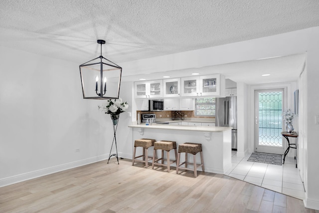 kitchen with white cabinetry, hanging light fixtures, light hardwood / wood-style flooring, appliances with stainless steel finishes, and kitchen peninsula